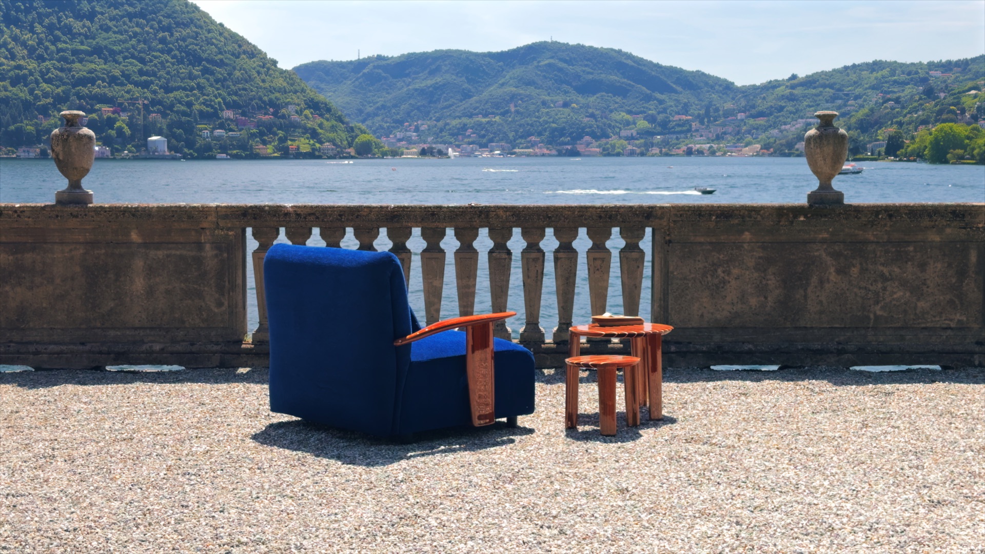 Blue armchair and wooden side table from Massimo Castagna’s Exteta × Riva collection, facing the lake