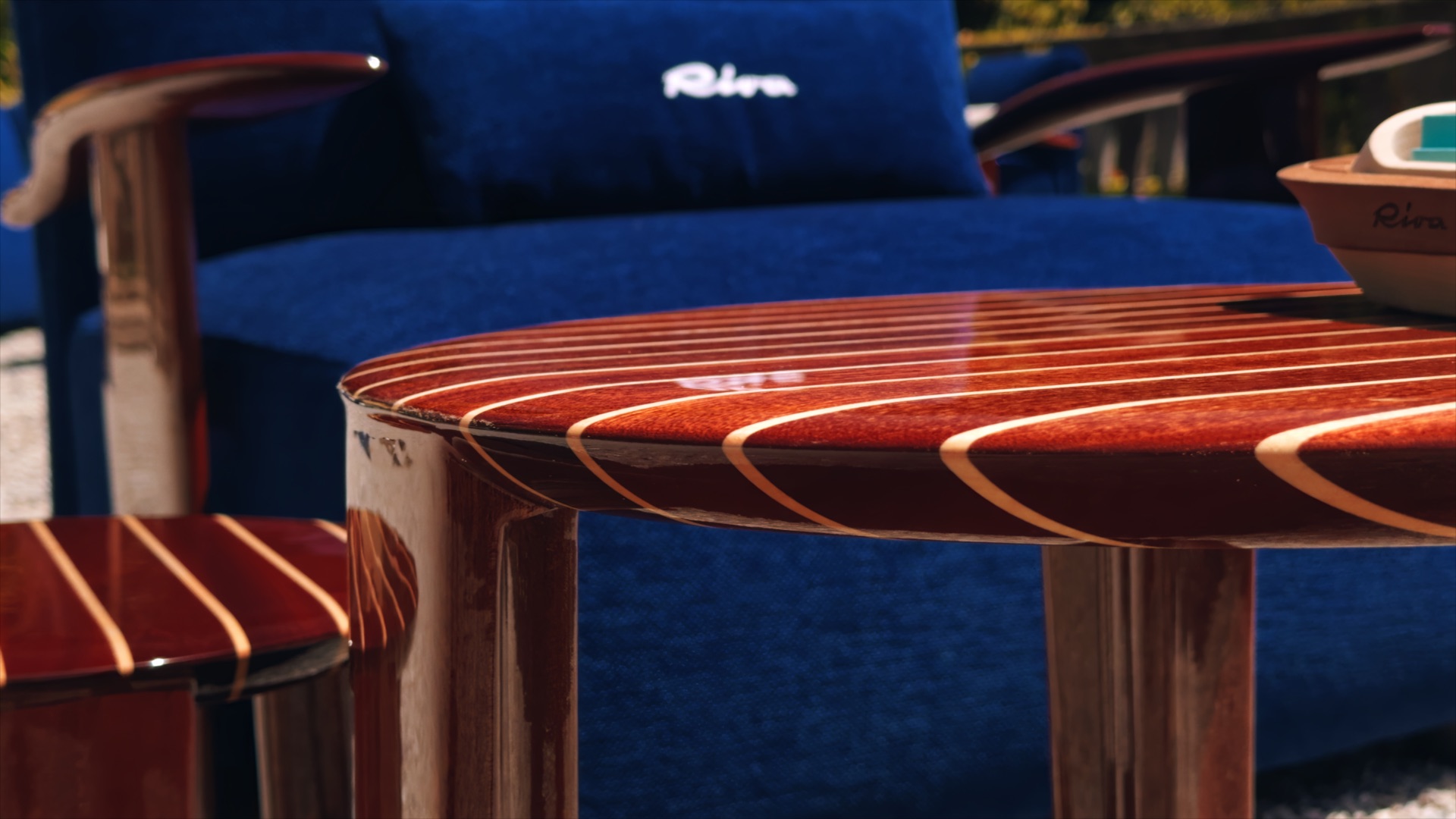 Varnished striped table from Massimo Castagna’s Exteta × Riva collection, beside blue seating