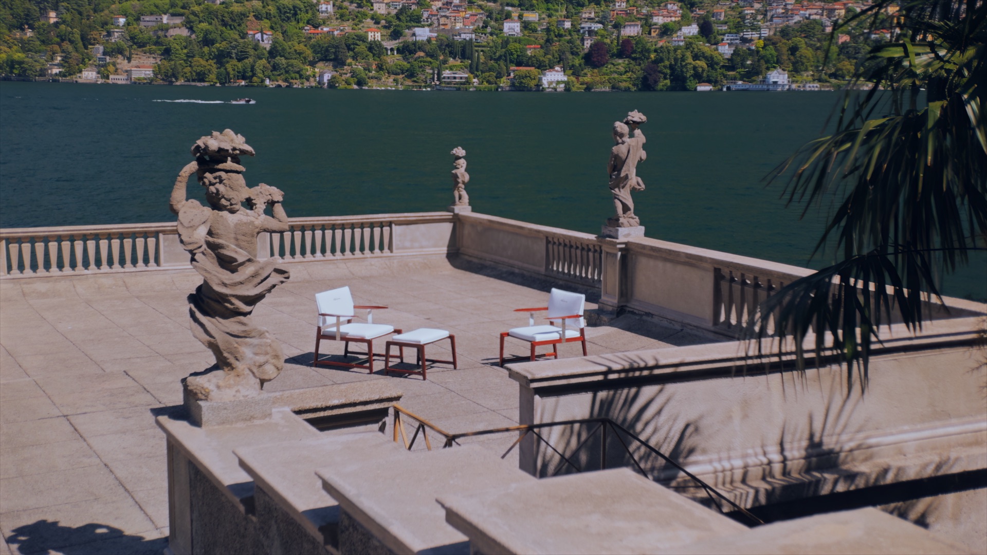 Furniture from Massimo Castagna’s Exteta × Riva collection on a lakeside terrace with stone statues