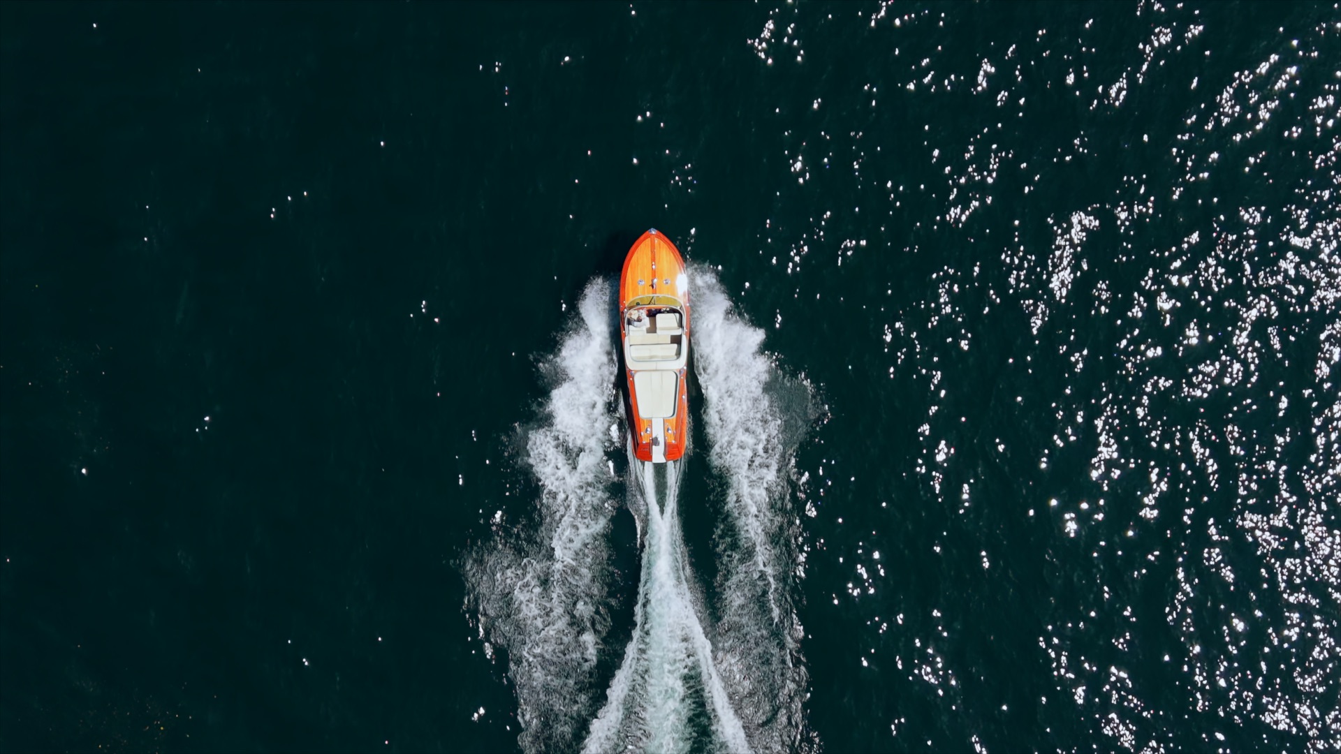 Riva boat seen from directly above, leaving a white wake across Lake Como