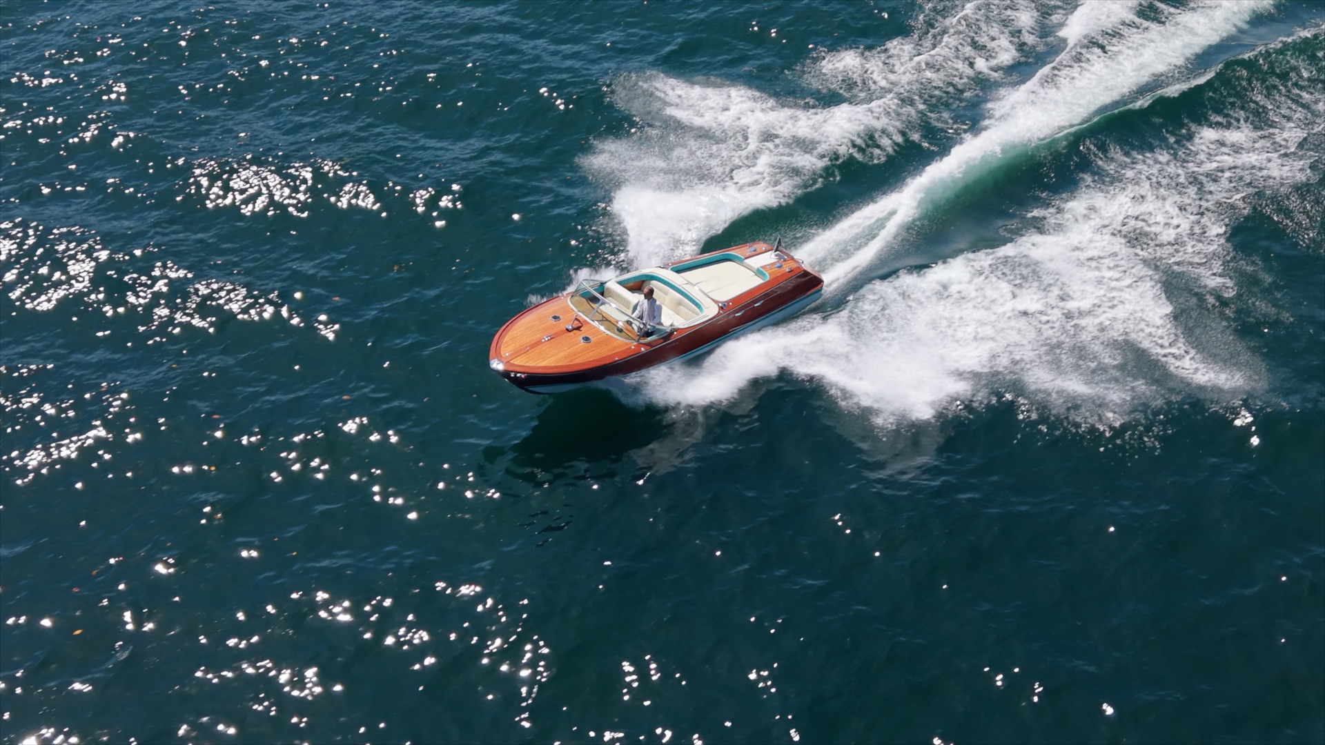 Riva boat turning across Lake Como with a curved white wake